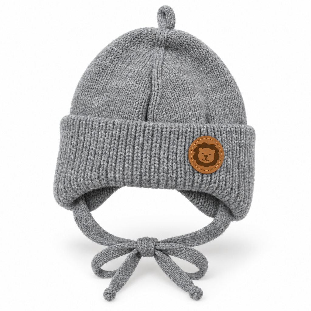 Grey knitted baby cap with lion patch, chunky ribbed cuff, ear flaps and tie strings – front view