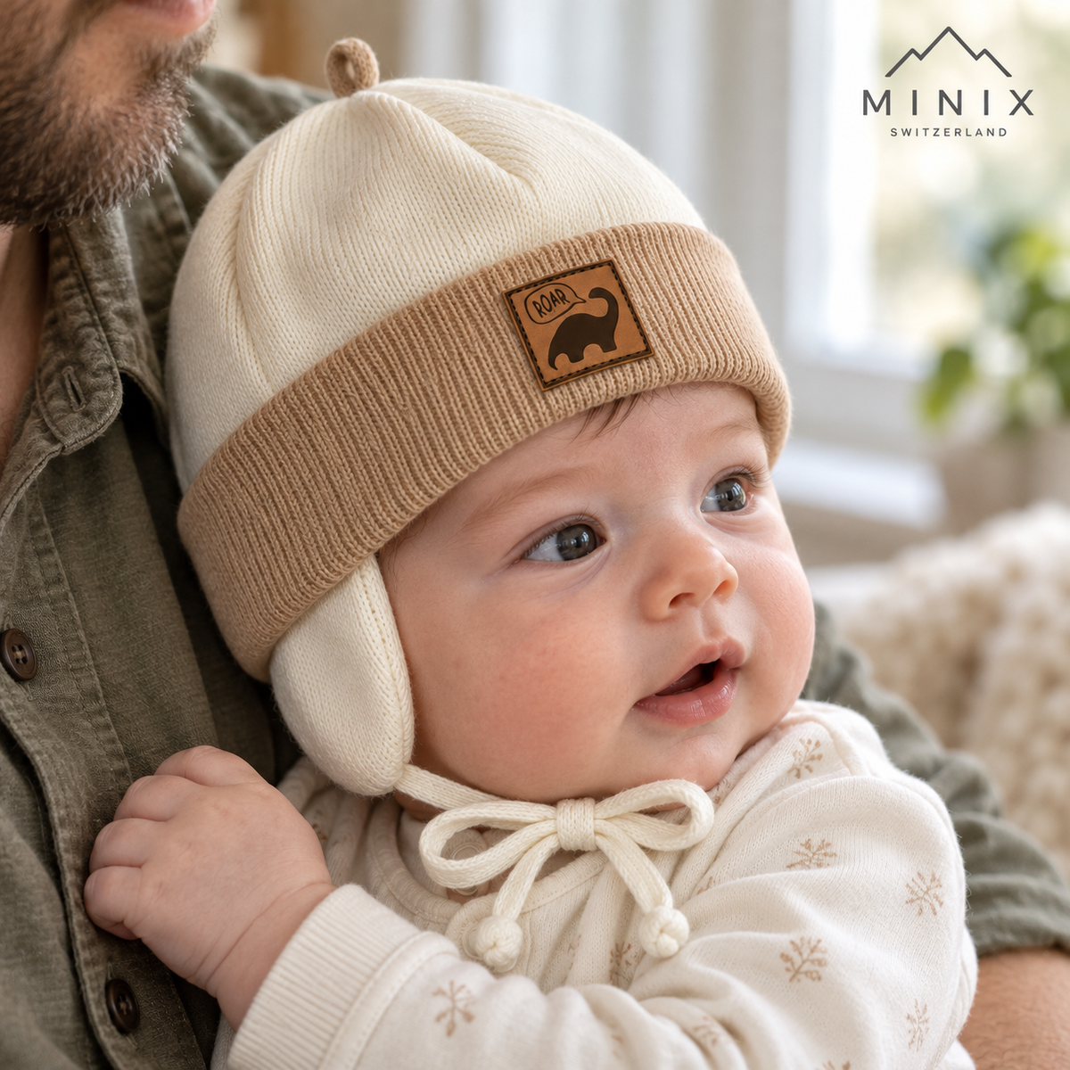 Baby in his father's arms wearing the cream and beige MINIX knitted dino cap