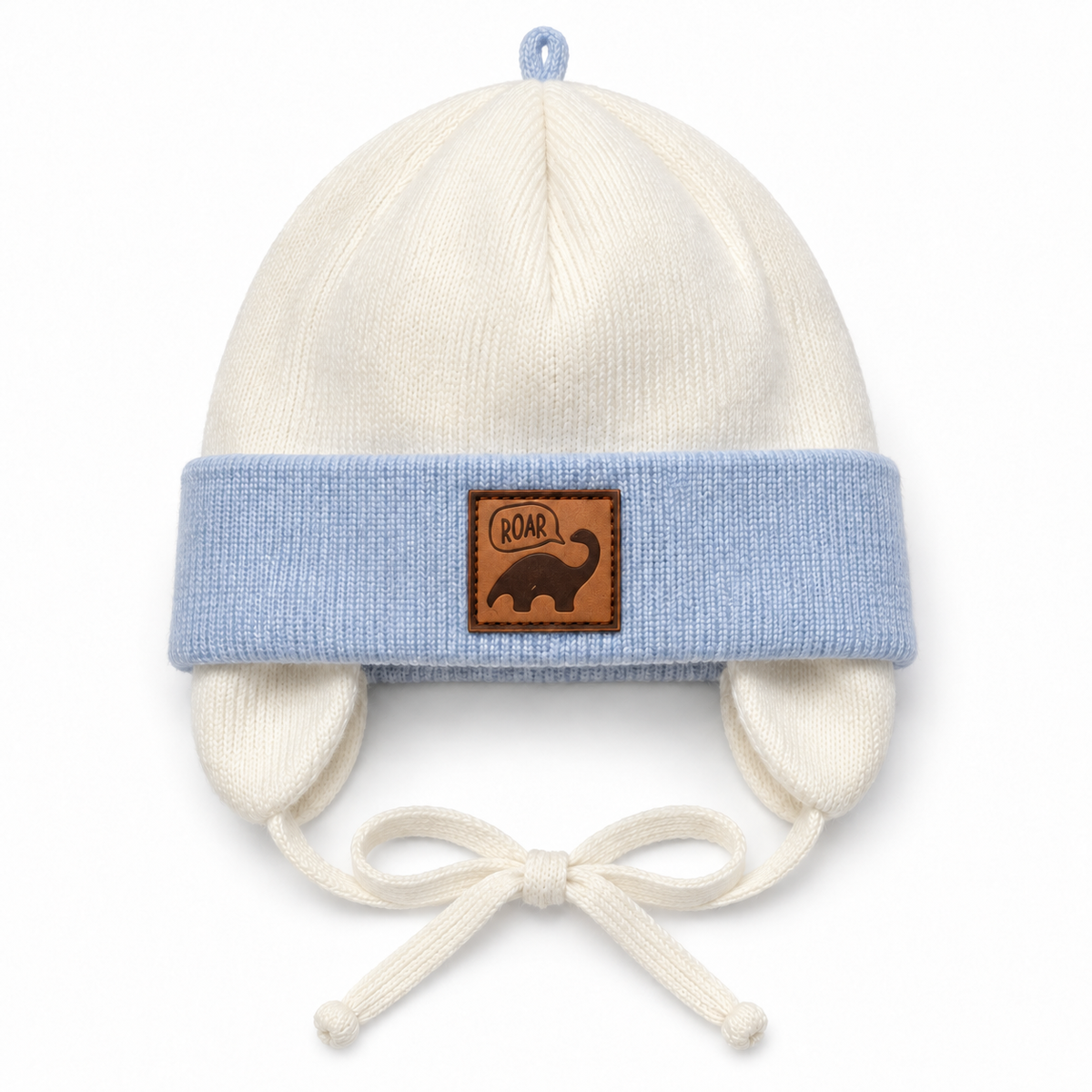 Cream knitted baby boy cap with light blue cuff, ROAR dino patch, ear flaps and tie strings – front view