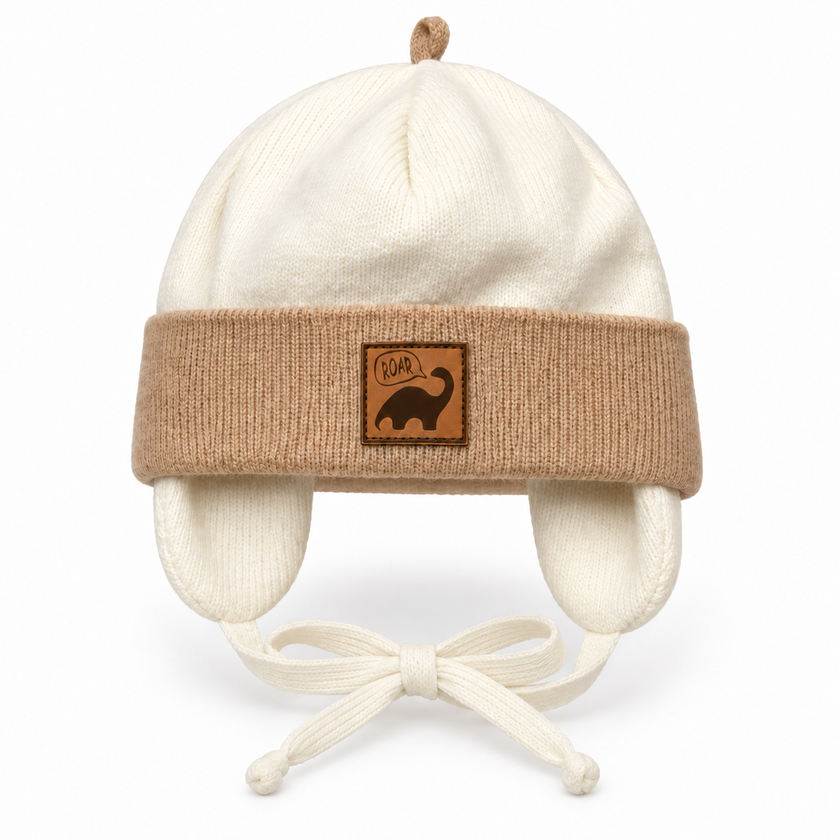 Cream knitted baby boy cap with beige cuff, ROAR dino patch, ear flaps and tie strings – front view