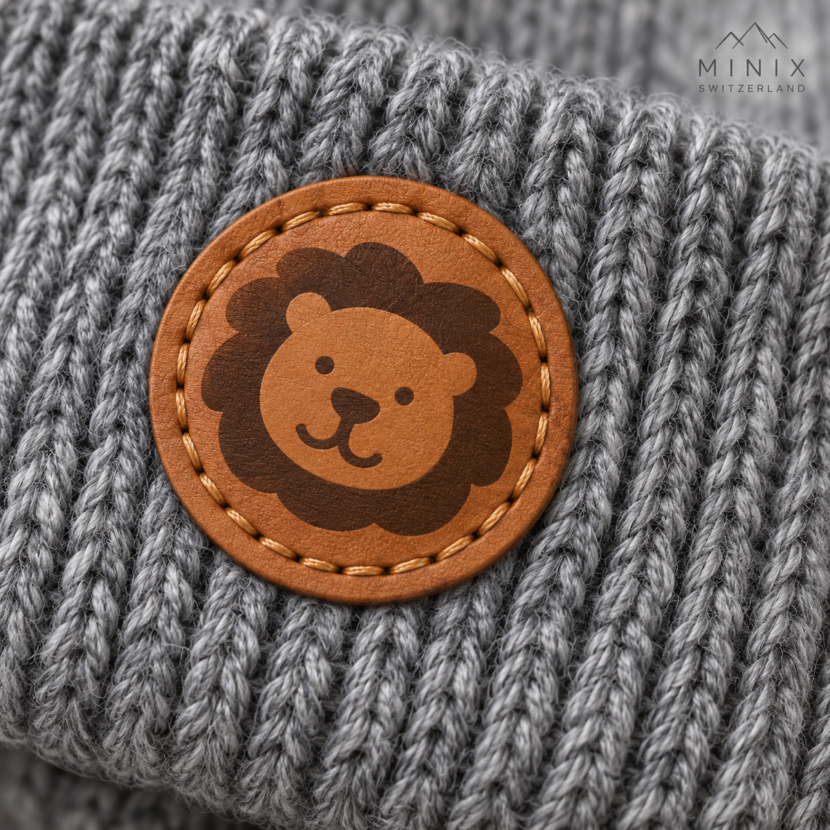 Grey knitted baby cap with lion patch and tie strings – flat lay
