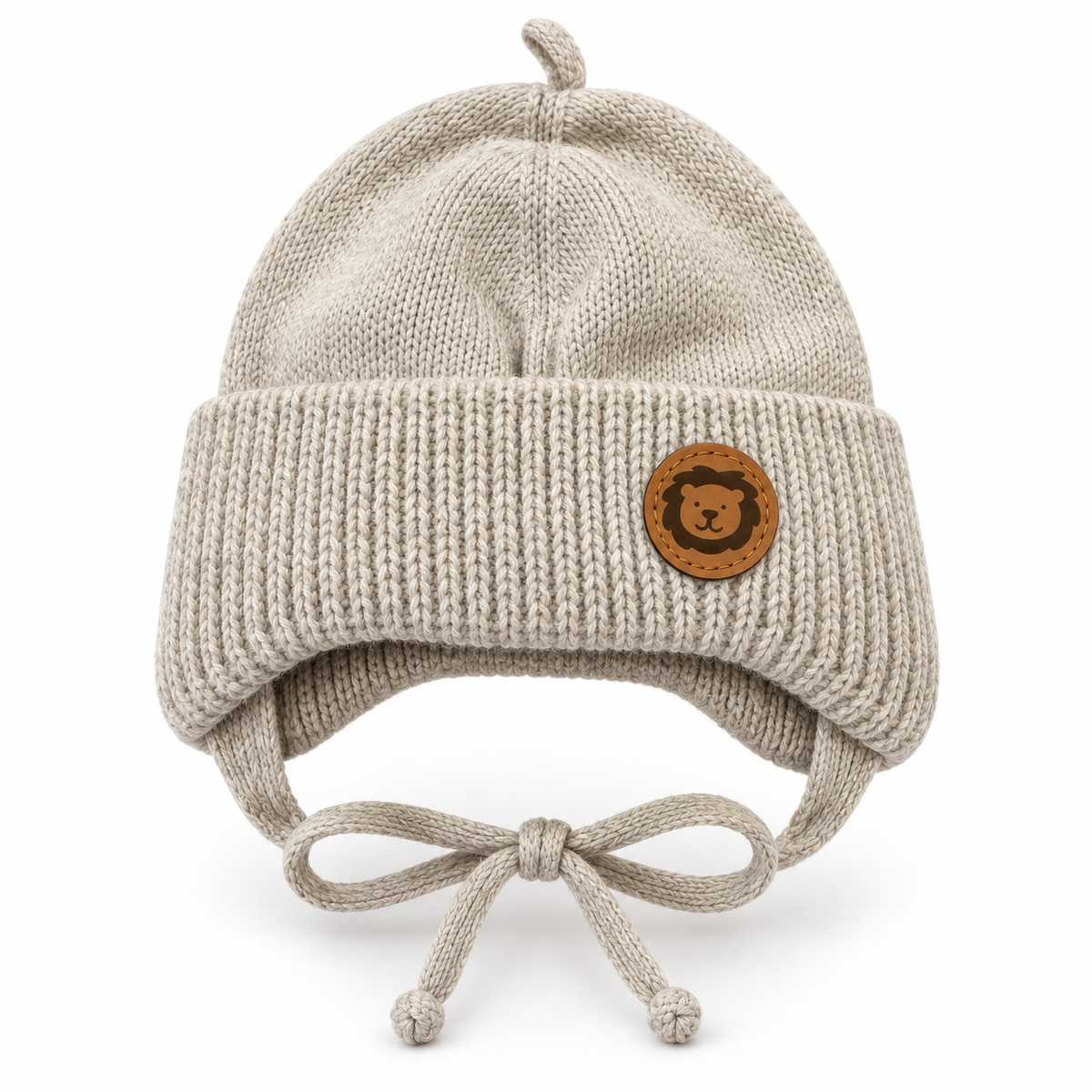 Beige knitted baby cap with lion patch, chunky ribbed cuff, ear flaps and tie strings – front view