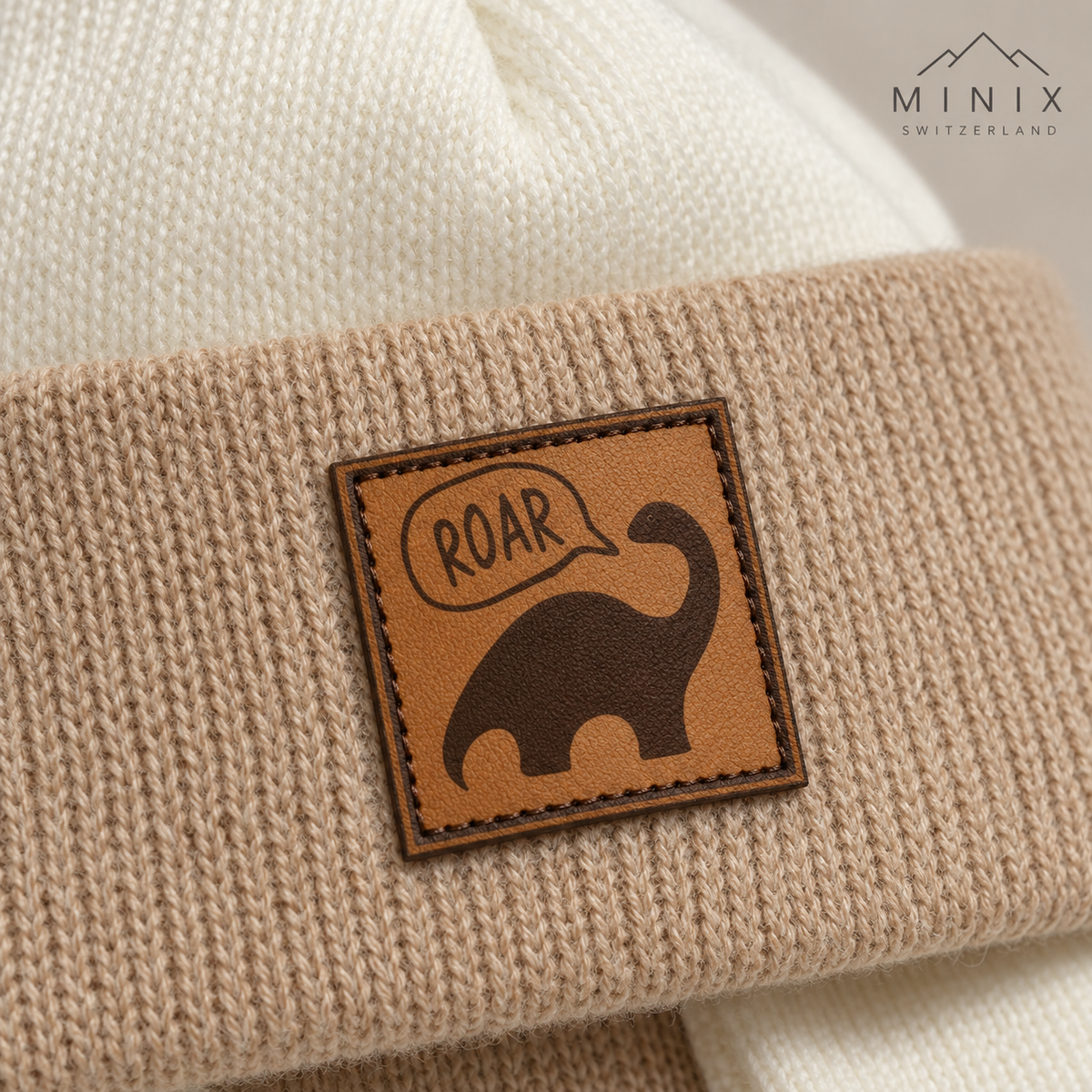 Cream and beige knitted baby cap with dino patch and ear flaps – angled view