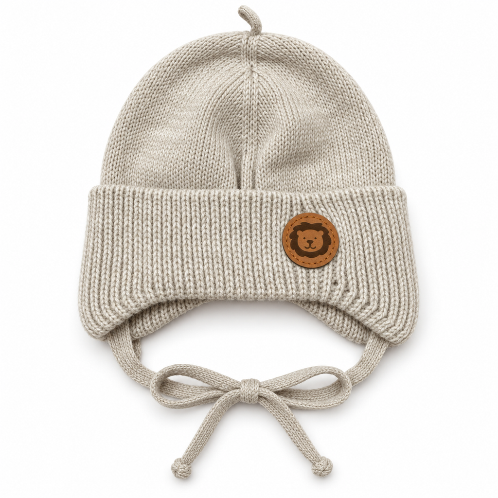 Beige knitted baby cap with lion patch, ear flaps and bow ties – flat front view