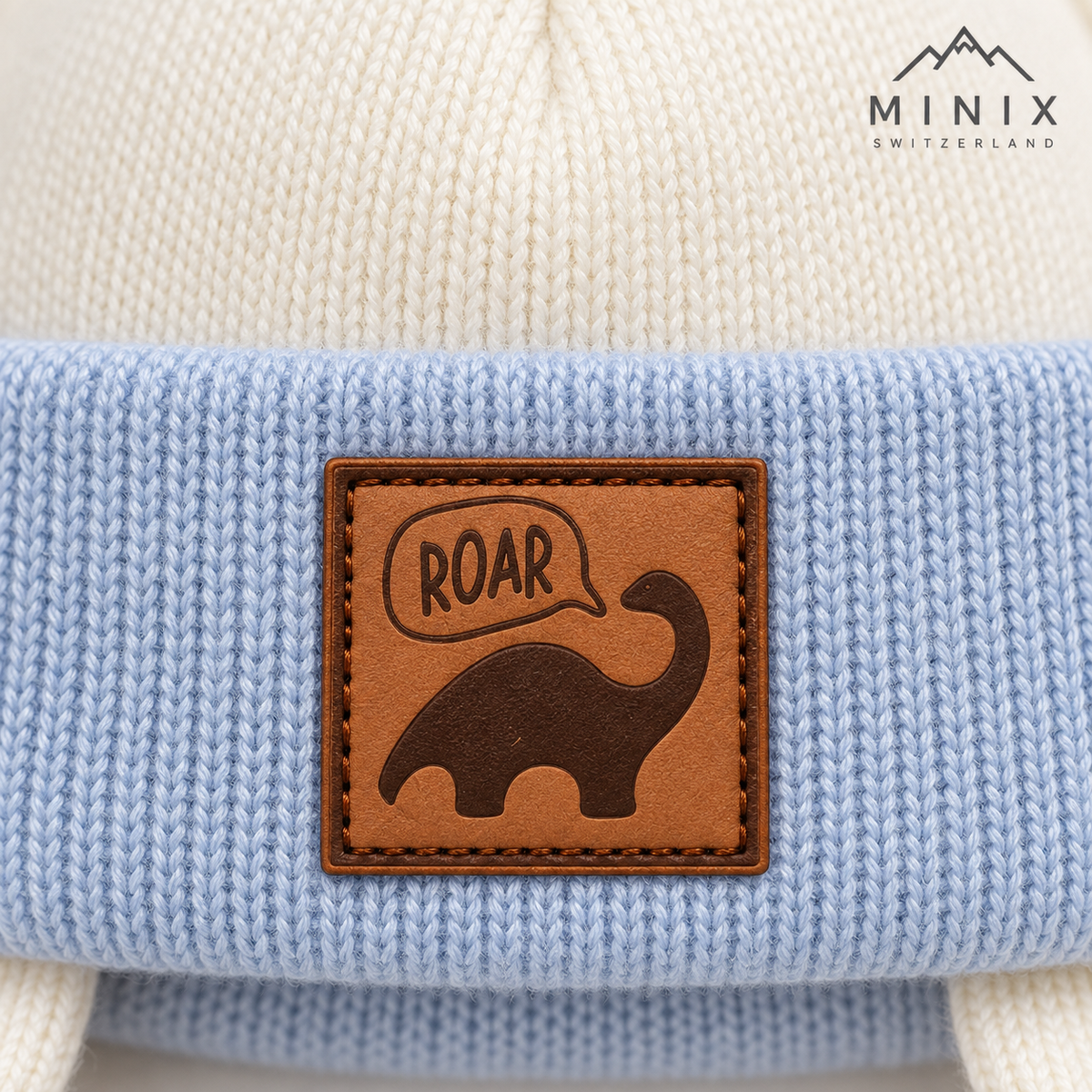 Close-up of the ROAR dinosaur leather-look patch on the light blue knitted cuff
