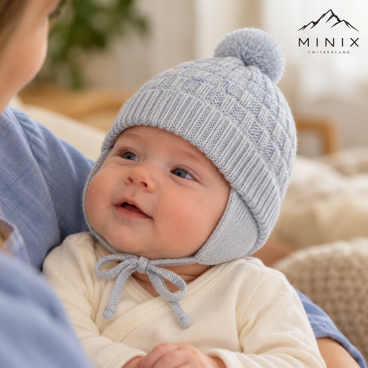Baby boy in a parent's arms wearing the light blue MINIX knitted pompom cap