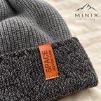 Close-up of the Space Adventure tag and charcoal mélange cuff on the grey knitted beanie