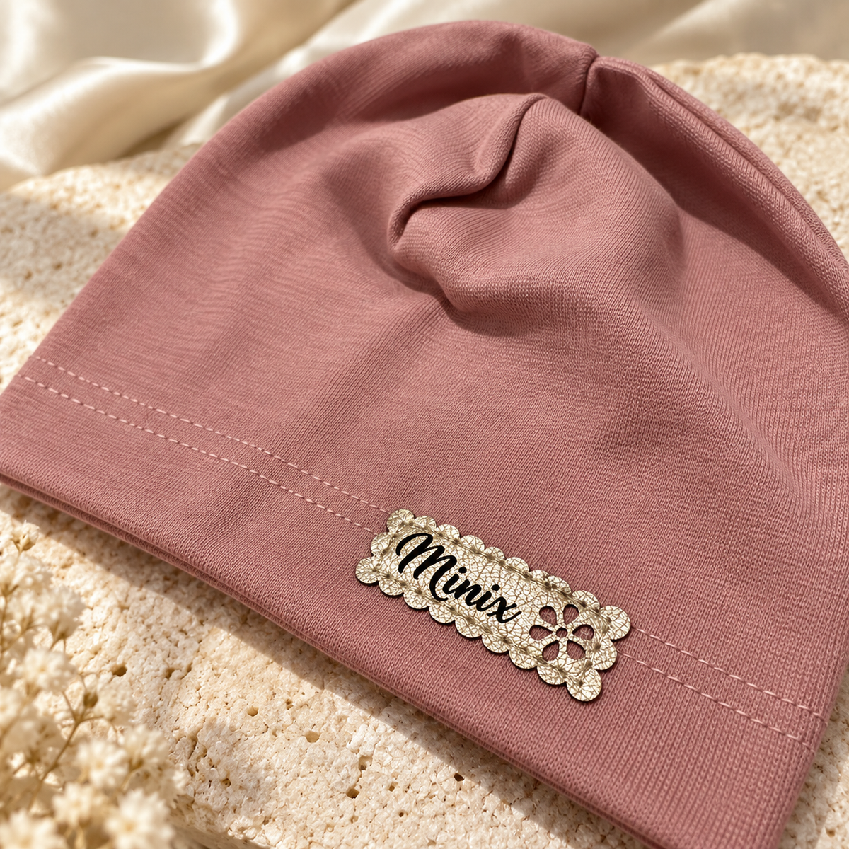 Close-up of the gold scalloped MINIX label with flower on a dusty rose kids cotton beanie