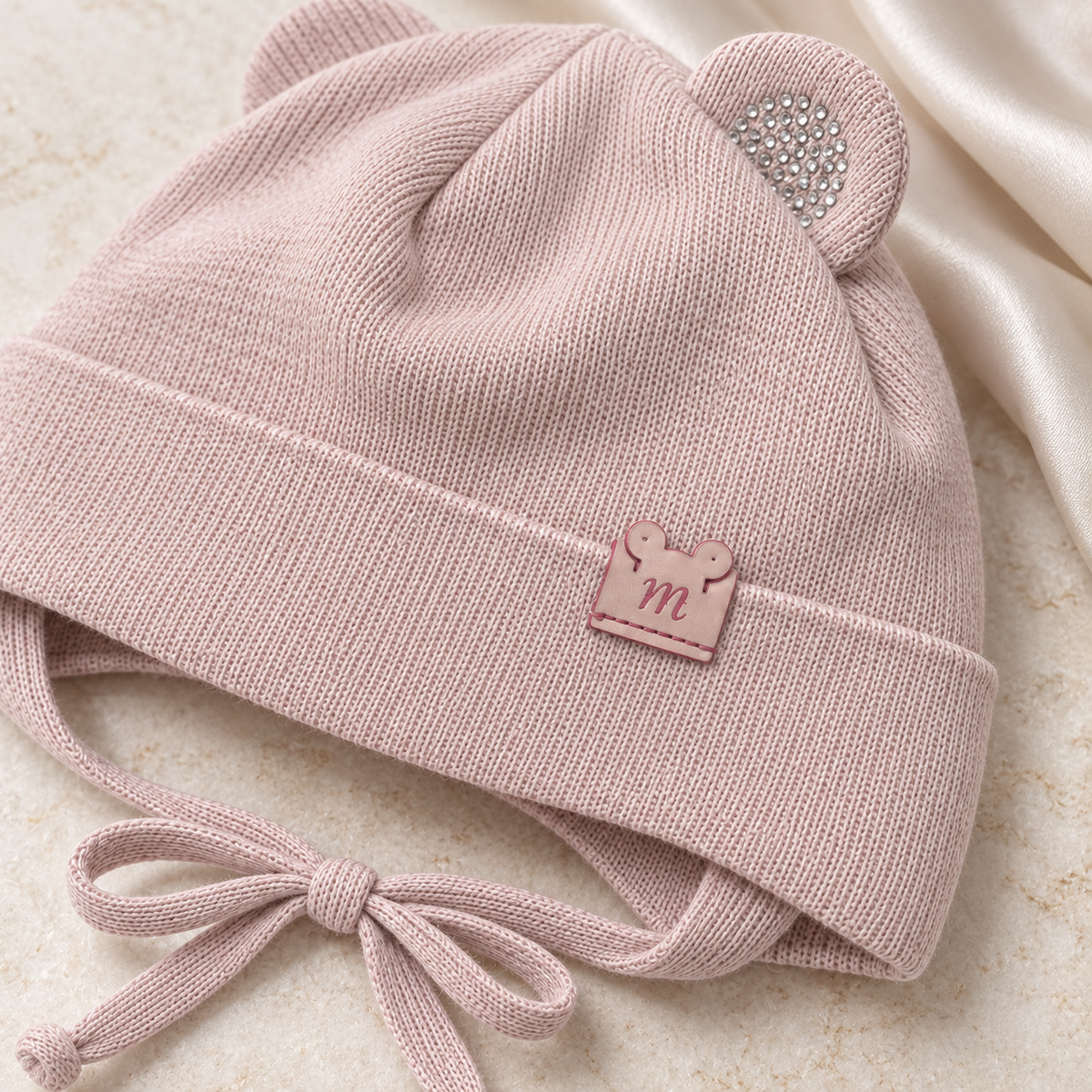 Close-up of the sparkly ear and little m patch on the dusty pink knitted baby cap