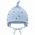 Boy wearing light blue sailboat print cotton cap with knot and ear covers on a sailboat