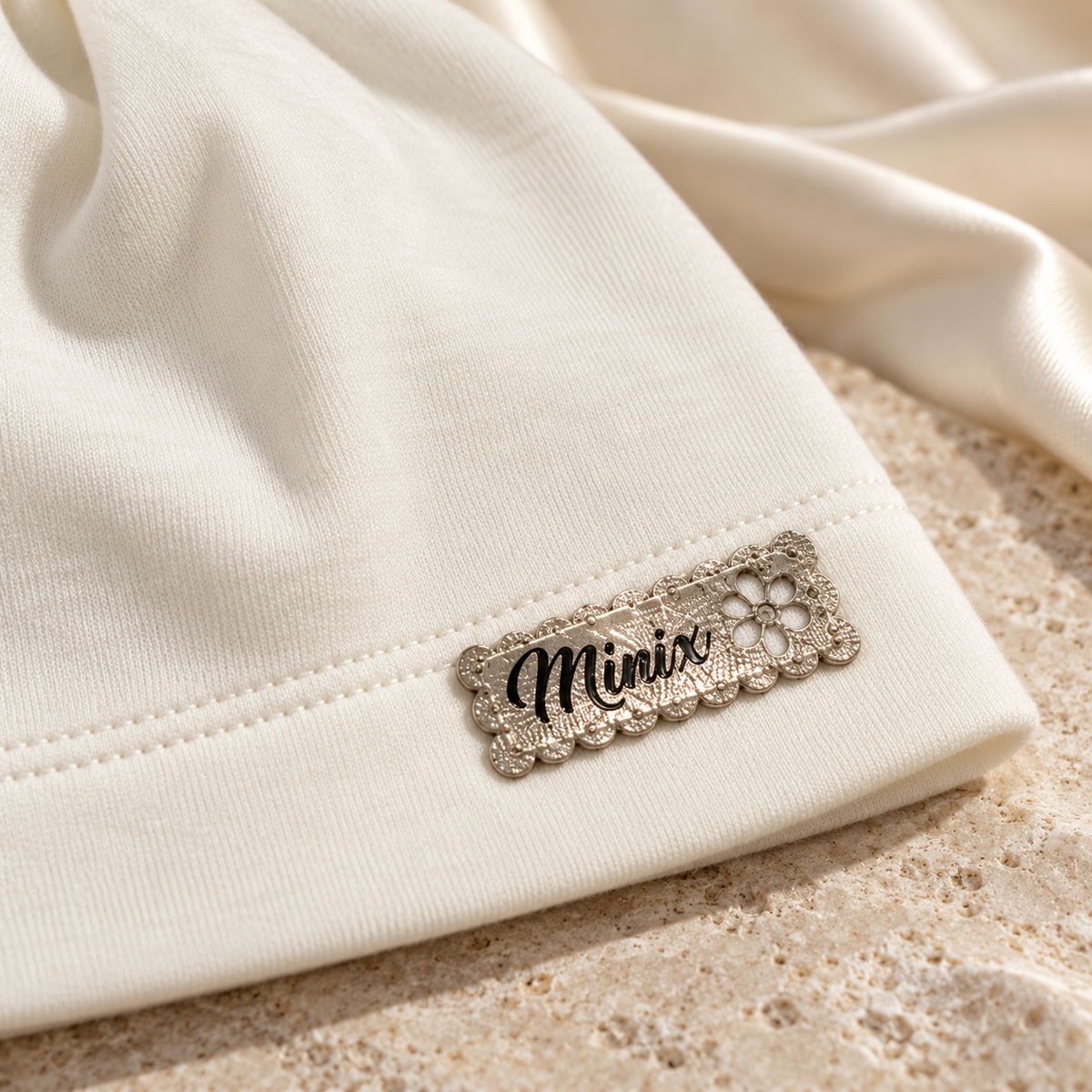 Close-up of the gold scalloped MINIX label with flower on a cream kids cotton beanie
