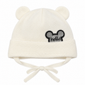 Cream knitted baby cap with bear ears, sparkly hello patch and tie strings – front view