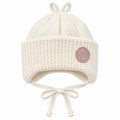Cream knitted baby girl cap with pink butterfly patch, chunky ribbed cuff, ear flaps and tie strings – front view