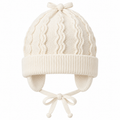 Cream wave-knit baby cap with knitted bow, fold-over cuff, ear flaps and tie strings – front view