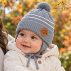 Smiling baby boy in a parent's arms wearing the grey MINIX Little Man knitted pompom cap