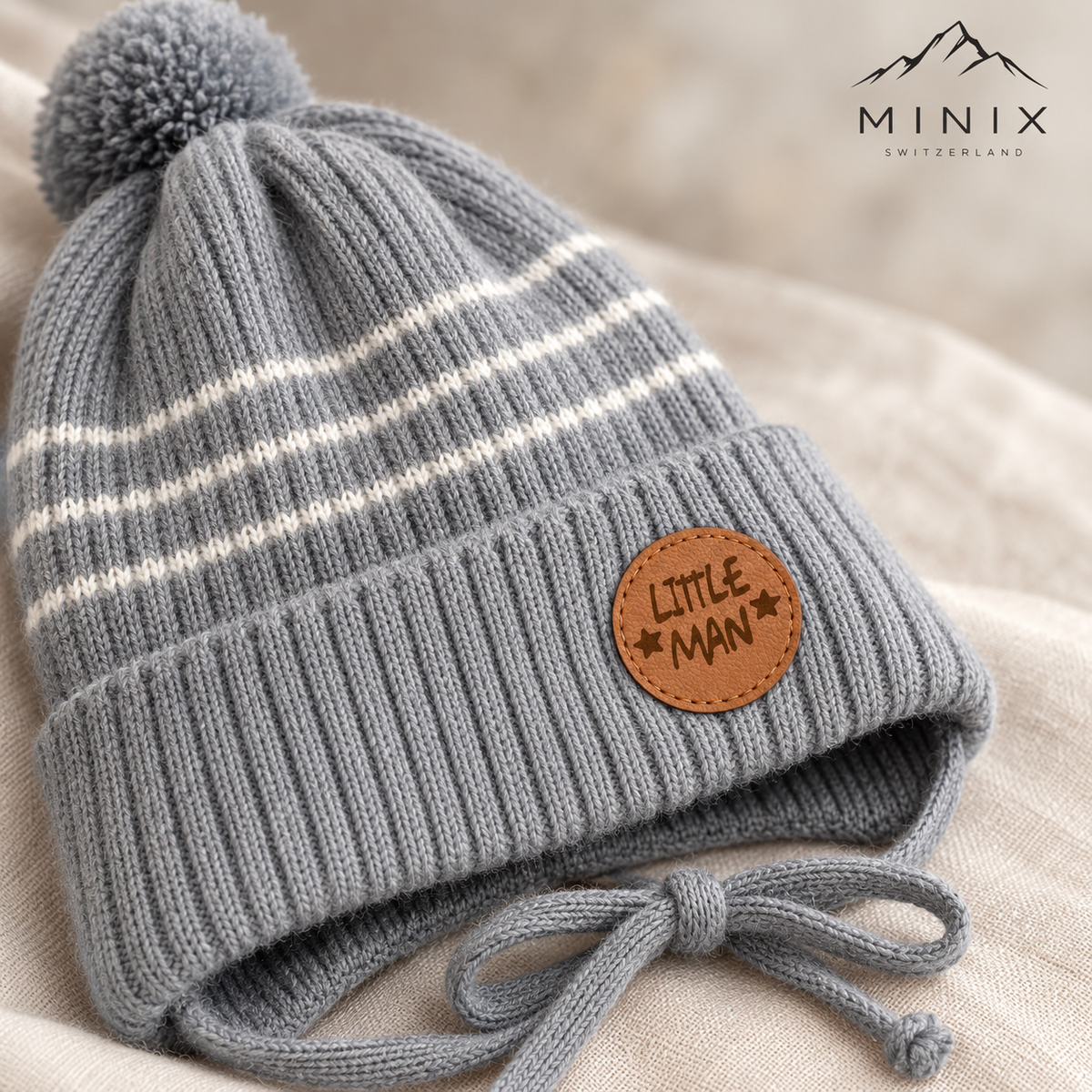 Close-up of the round Little Man patch, ribbed cuff and cream stripes on the grey knitted cap
