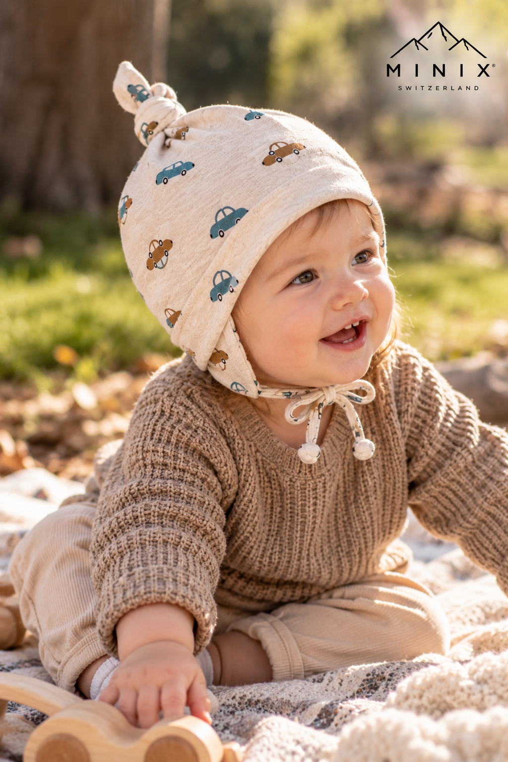 Toddler wearing the beige MINIX cotton cap with car print and ear flaps