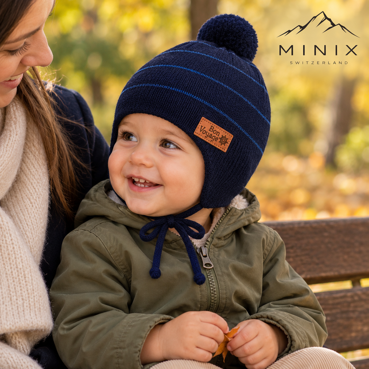 Smiling baby boy on a parent's lap wearing the navy MINIX striped knitted pompom cap