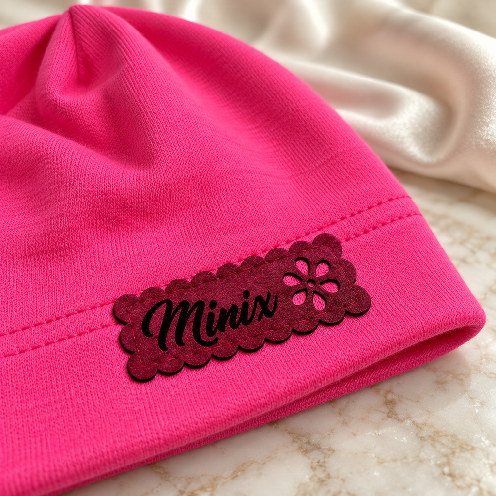 Close-up of the scalloped felt MINIX label with flower cut-out on a hot pink kids cotton beanie