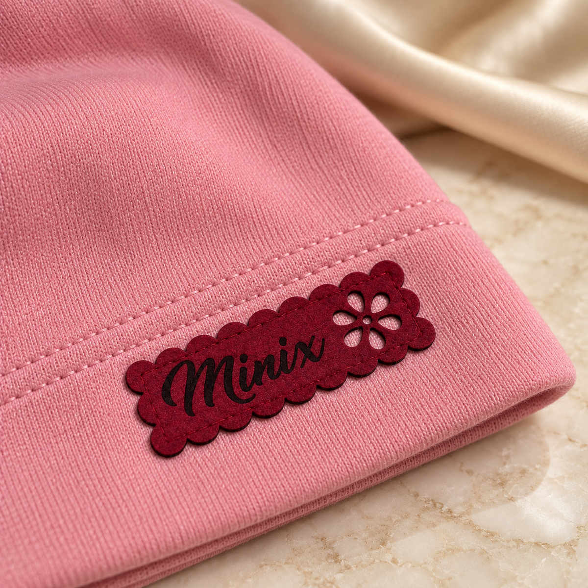 Close-up of the hot pink scalloped MINIX label with flower cut-out on a pink kids cotton beanie
