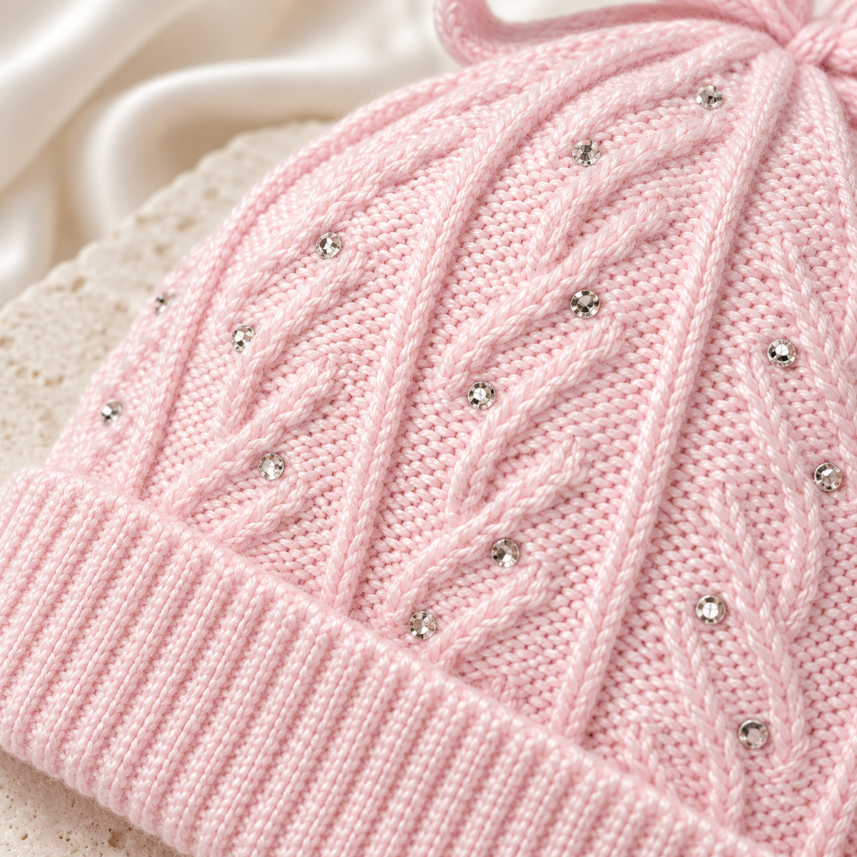 Close-up of the cable knit and rhinestone details on a light pink baby girl cap